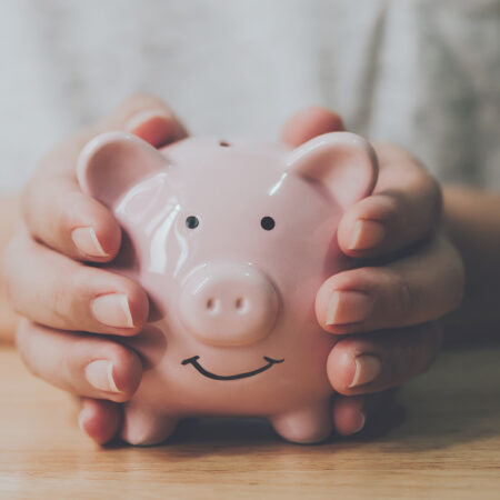 Person with hands around a pink ceramic piggy bank